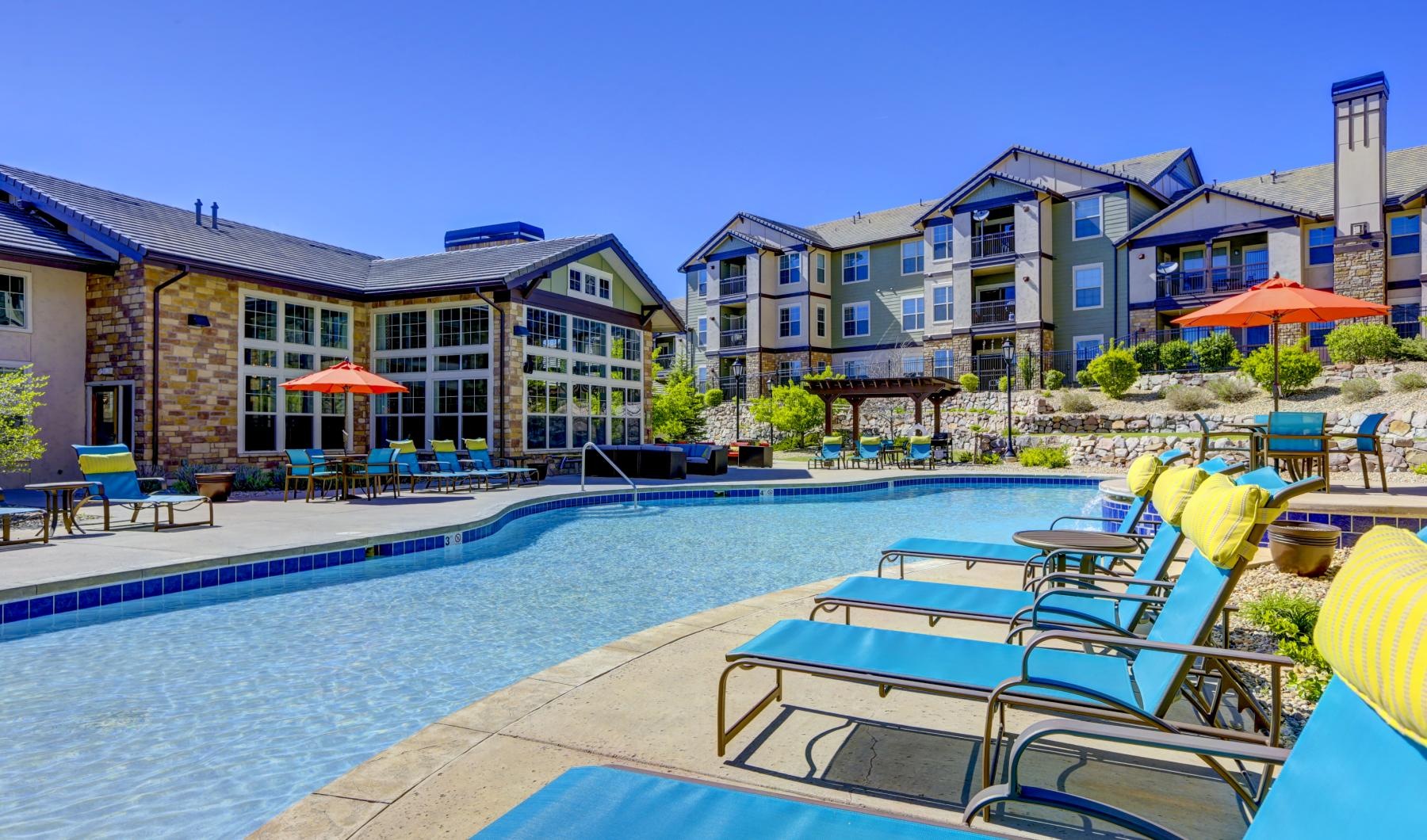 a pool with lounge chairs and umbrellas by a building