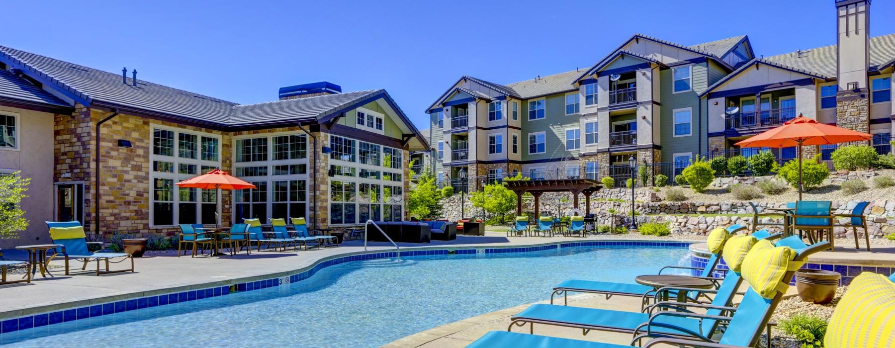 a pool with lounge chairs and umbrellas by a building